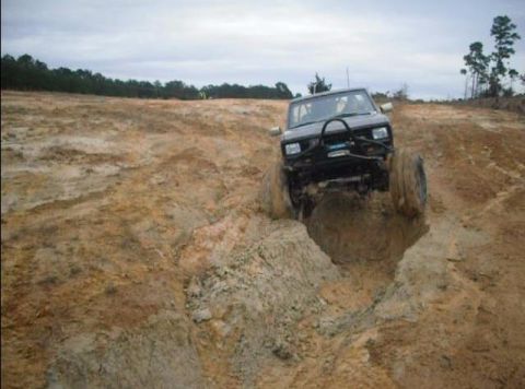 1984 Ford Bronco II - A black SUV navigates a challenging off-road terrain with a muddy ditch.