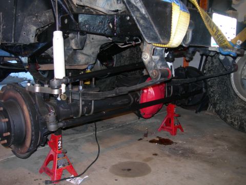 1991 Jeep Wrangler - The front axle and suspension of a vehicle are visible, supported by jack stands, with red brake calipers and a white shock absorber.