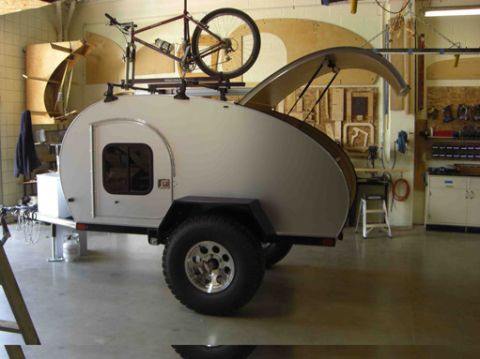 1991 Ford Bronco - A teardrop trailer is parked inside a workshop, with a bicycle mounted on its roof rack.