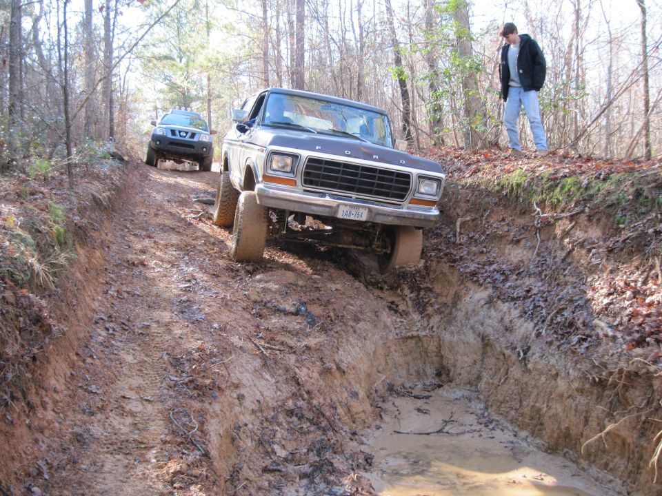 Lifted Ford pickup descending a deep eroded dirt trail in the woods