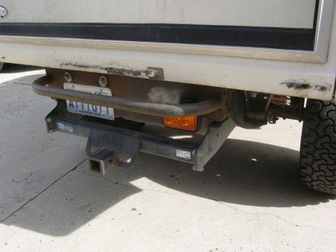 1986 Ford Bronco - The rear of a white SUV shows a trailer hitch and a rusty bumper bar.