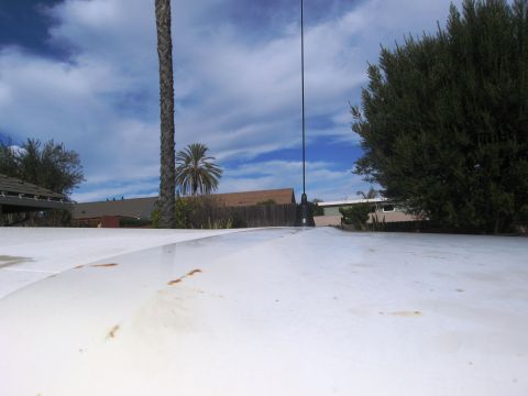 1986 Ford Bronco - View from the roof of a vehicle, showing an antenna and surrounding trees and houses.