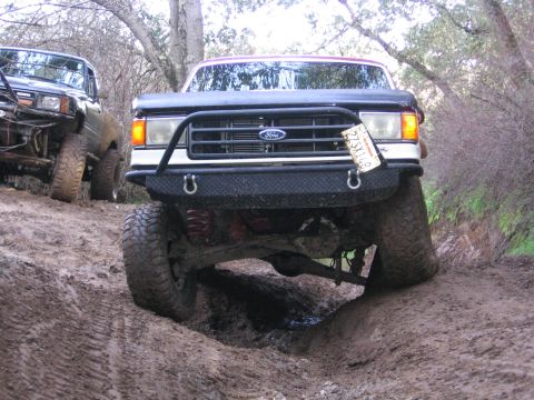 1989 Ford Bronco - This Ford truck navigates a challenging muddy terrain with another vehicle nearby.