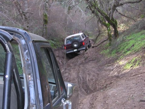 1989 Ford Bronco - Two vehicles navigate a steep, muddy trail through a wooded area.