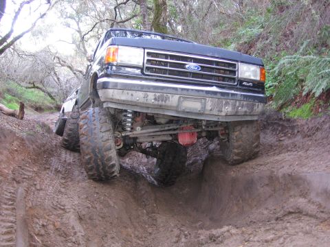 1989 Ford Bronco - A black Ford Bronco is shown off-roading through a muddy terrain.