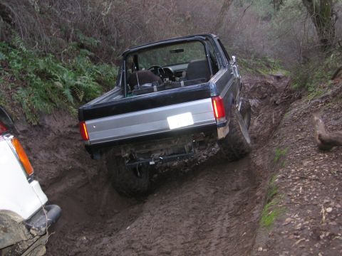 1989 Ford Bronco - A black Ford Bronco navigates a difficult muddy trail, with another vehicle visible to the left.