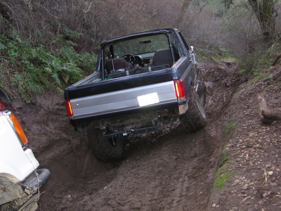 Black Ford Bronco with silver trim on a muddy trail, rear view