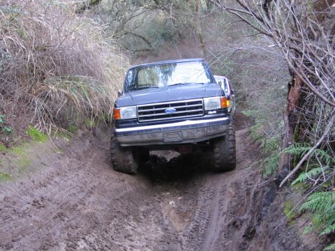 1989 Ford Bronco - This Ford F-series truck navigates a challenging muddy path, with another vehicle following closely behind.