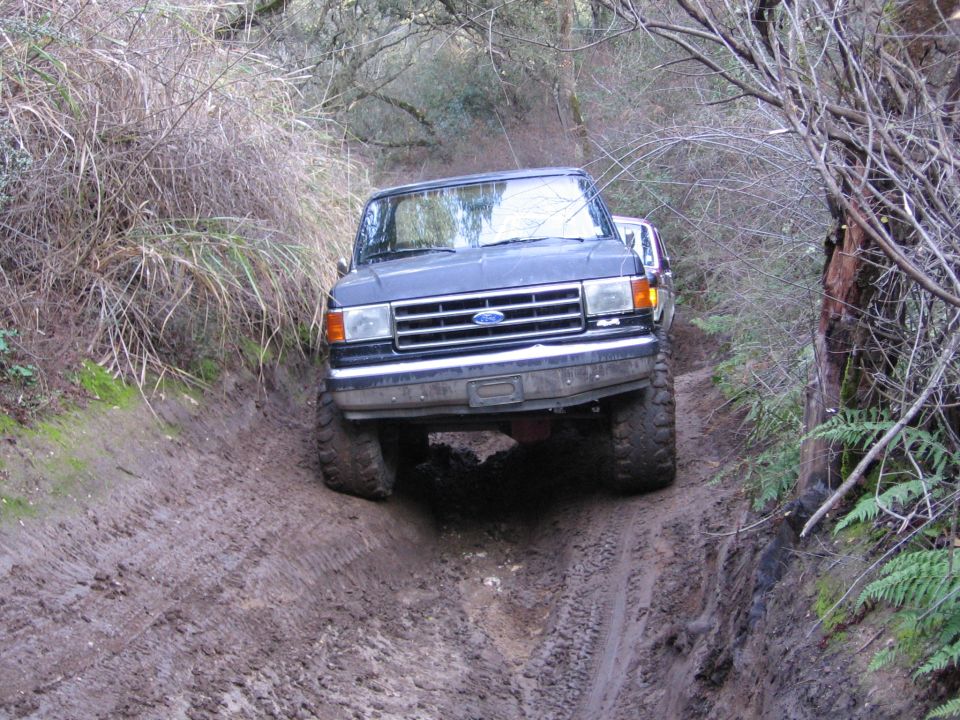 Dark blue Ford F-series truck going down a muddy trail. Another vehicle is behind it