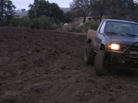 1989 Ford Bronco - A dark pickup truck navigates a muddy terrain, its headlights illuminating the path ahead.