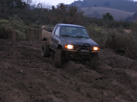 1989 Ford Bronco - Pickup truck navigating a muddy terrain with its headlights on.