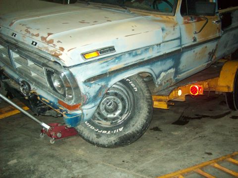 1971 Ford F-100 - A rusty Ford truck is being loaded onto a trailer, showing its front quarter panel and wheel.