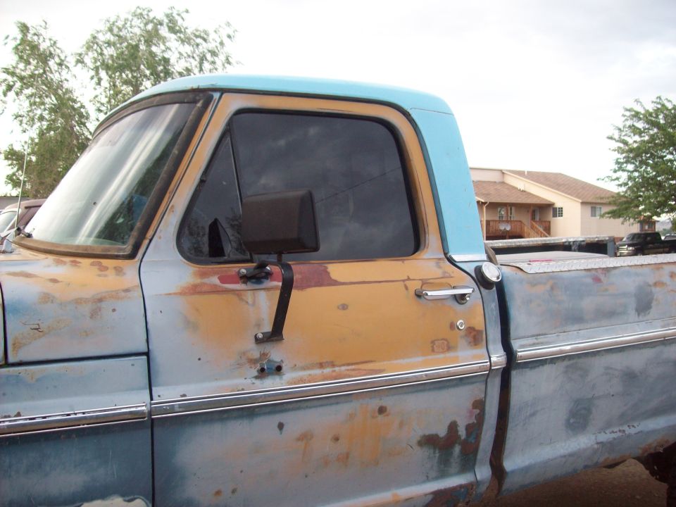 Side view of a rusty, two-tone blue and tan pickup truck with a light blue cab roof