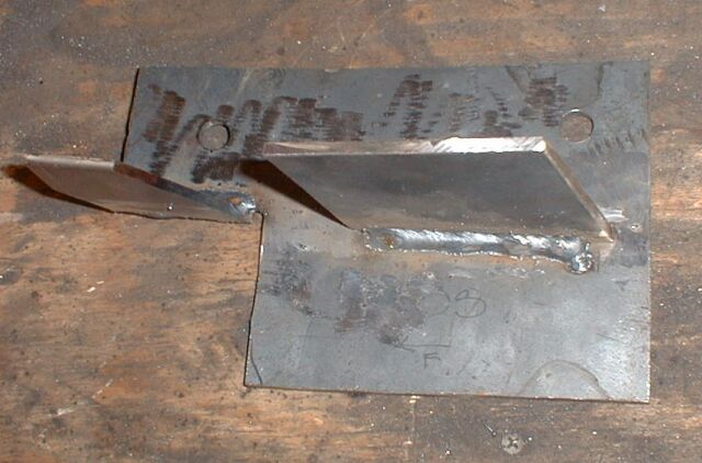 Two fabricated bare-metal welded brackets sitting on a workbench with chalk markings