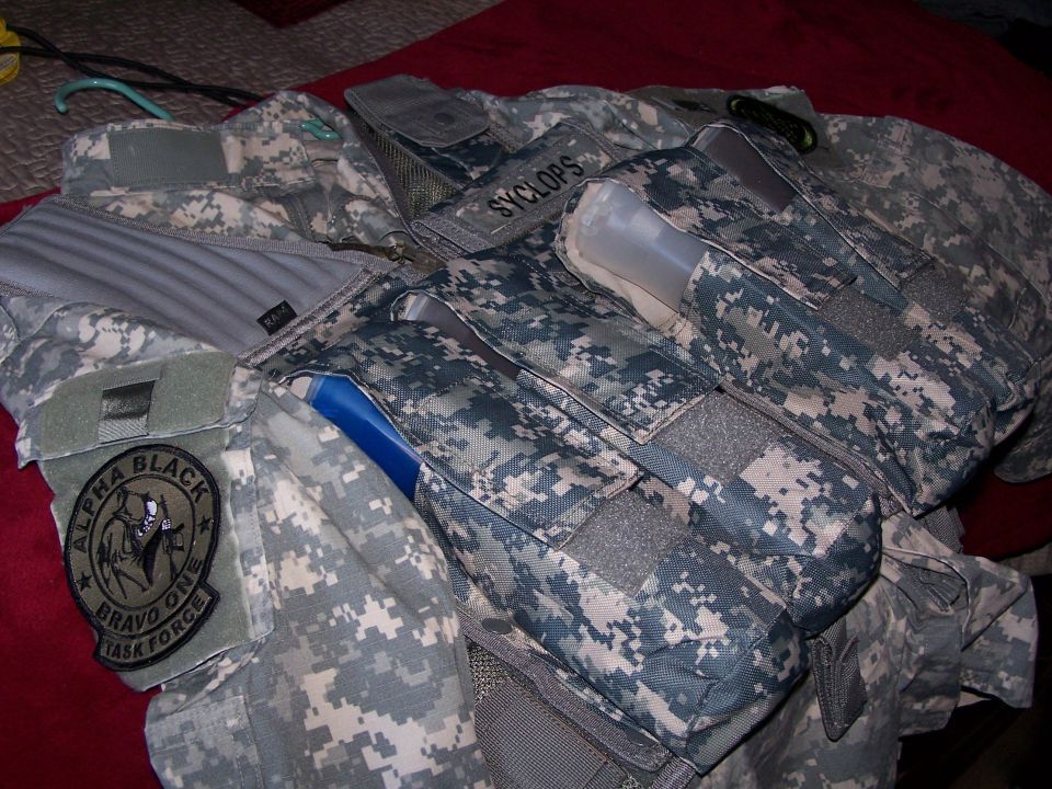 Tactical vest with digital camouflage pattern, pouches, and patches reading "SYCLOPS" and "ALPHA BLACK BRAVO ONE TASK FORCE"