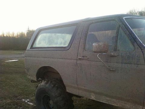 1990 Ford Bronco - This 1990 Ford Bronco is covered in mud, showing its side profile in an outdoor setting.