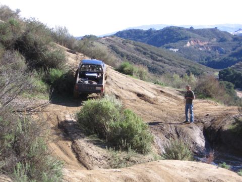 1989 Ford Bronco - A Toyota pickup truck navigates a challenging off-road trail in a hilly, arid landscape.
