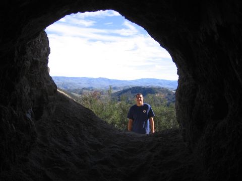 1989 Ford Bronco - View from inside a cave shows a man framed by the opening, with a landscape beyond.
