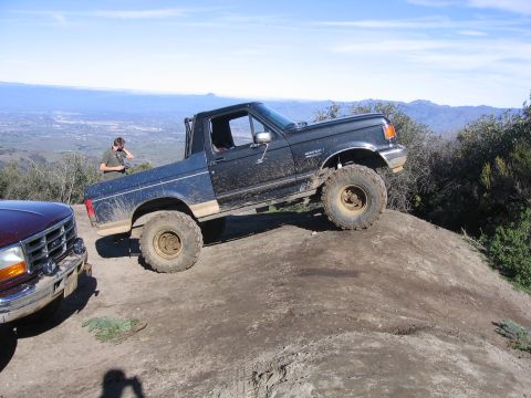 1989 Ford Bronco - A black Ford Bronco is shown off-roading on a dirt hill with another vehicle partially visible to the left.