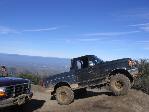 1989 Ford Bronco - A black 1989 Ford Bronco is parked on a dirt incline, with another vehicle visible to its left.