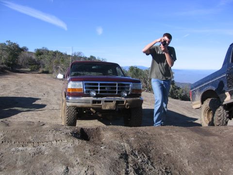 1989 Ford Bronco - A man photographs a maroon Ford F-150 truck on a dirt road with another truck nearby.