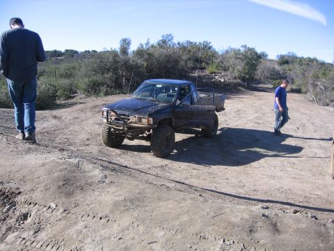1989 Ford Bronco - A black 1989 Ford Bronco sits on a dirt path with its driver's door ajar, surrounded by dry brush and clear skies.