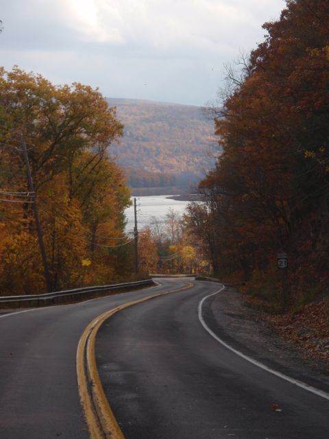 1968 Ford Mustang - A scenic autumn drive unfolds on a winding road, with colorful foliage framing a view of a lake and rolling hills.