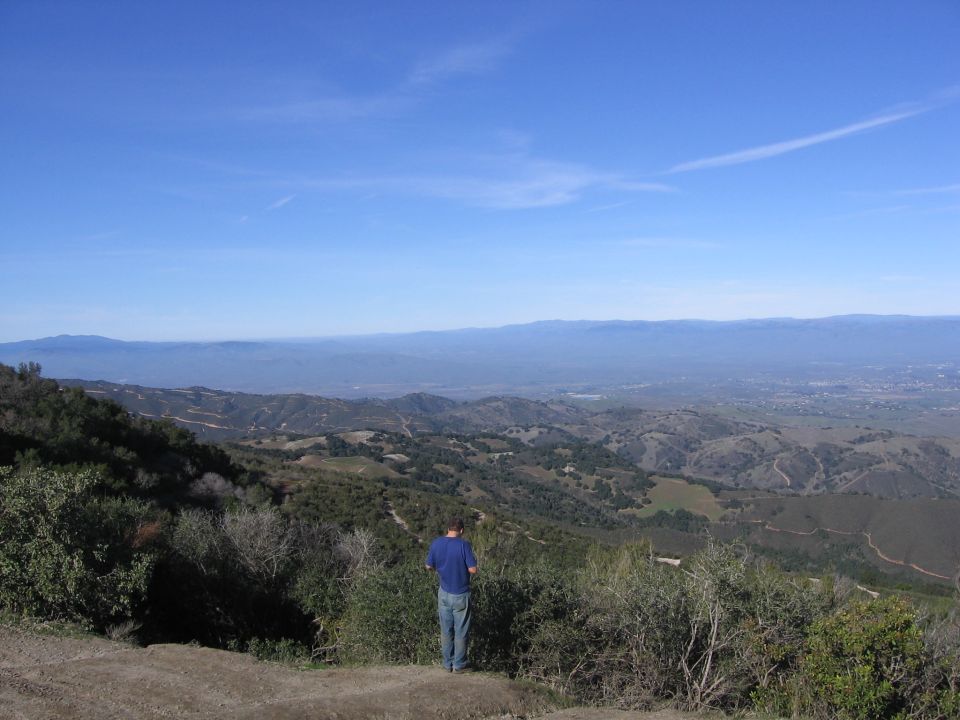 Man looking out over a vast, hilly landscape under a clear blue sky