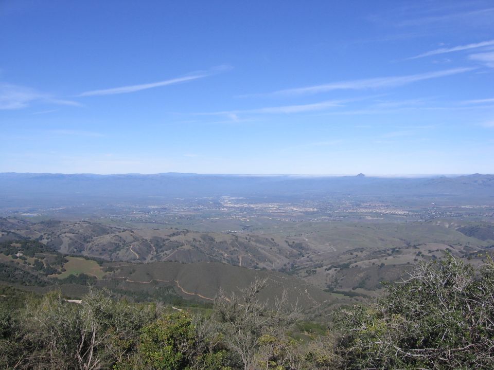 Overlook view of a valley with a town and distant mountains under a clear blue sky