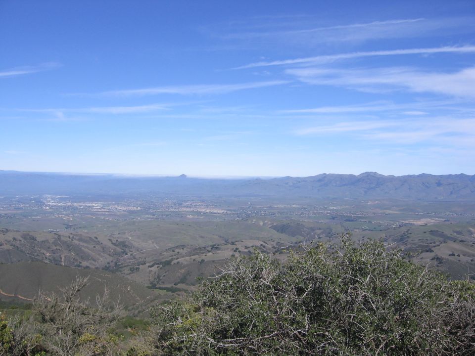 View from a hill overlooking a valley with a town and mountains in the distance