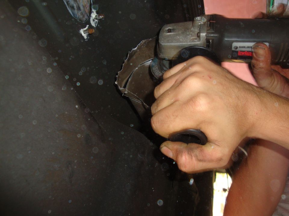 Black angle grinder cutting a curved metal panel