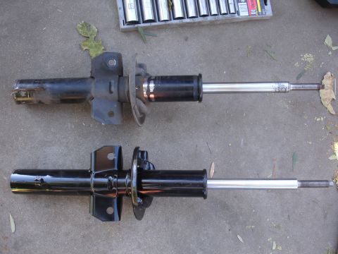 1992 Ford Taurus - A comparison of a used and a new car suspension strut is shown on a concrete surface.