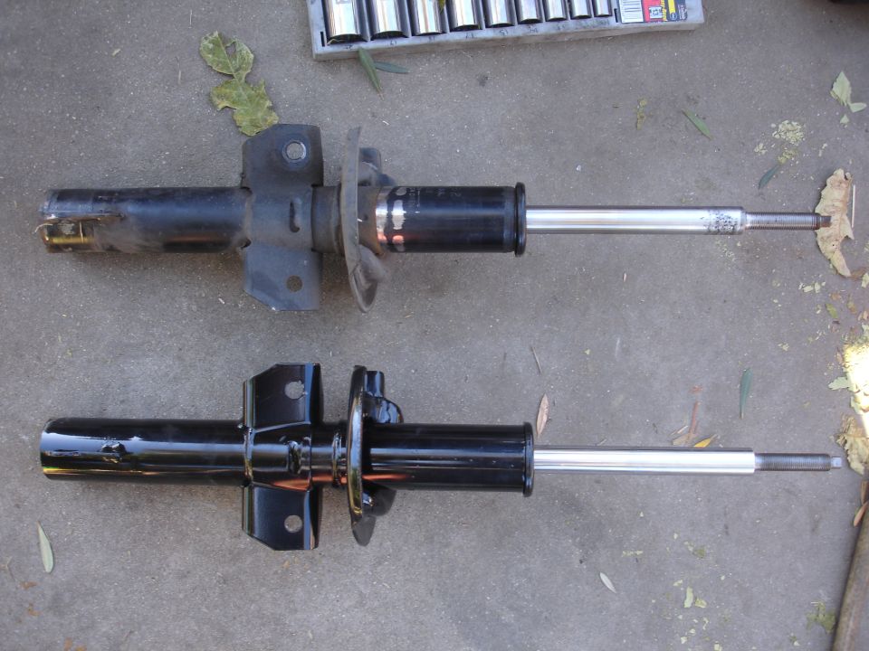 Two car suspension struts, one used and one new