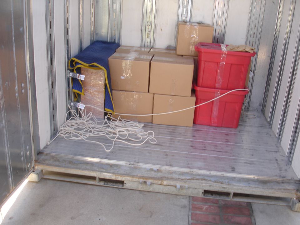 Interior of a cargo van filled with boxes, red bins, and moving blankets. A coiled rope lies on the floor