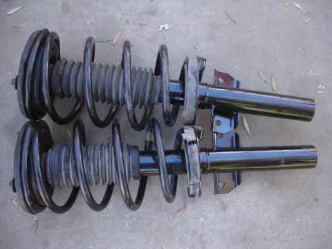 1992 Ford Taurus - Two front struts with integrated coil springs are laid out on a concrete surface.