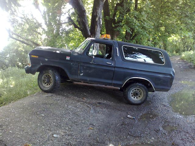 Black 1978 Ford Bronco SUV, side view, parked on a dirt path under trees