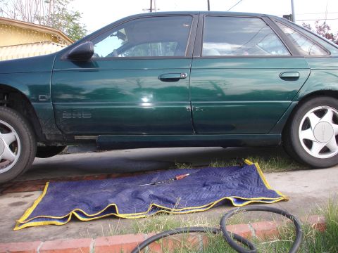 1995 Ford Taurus - Side view of a 1995 Ford Taurus parked outdoors with a blue moving blanket and tools laid out on the ground.