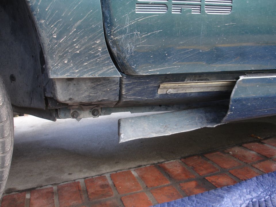 Green car door with visible scratches and mud, showing a damaged lower trim piece and part of a tire