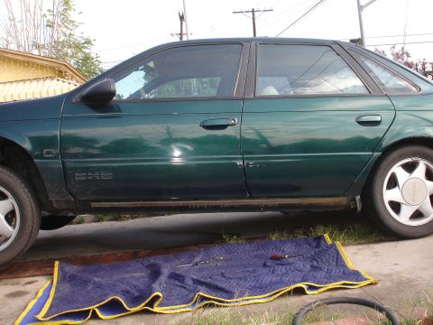 1995 Ford Taurus - A green 1995 Ford Taurus is parked outside with a blanket and tools laid out in front of it.