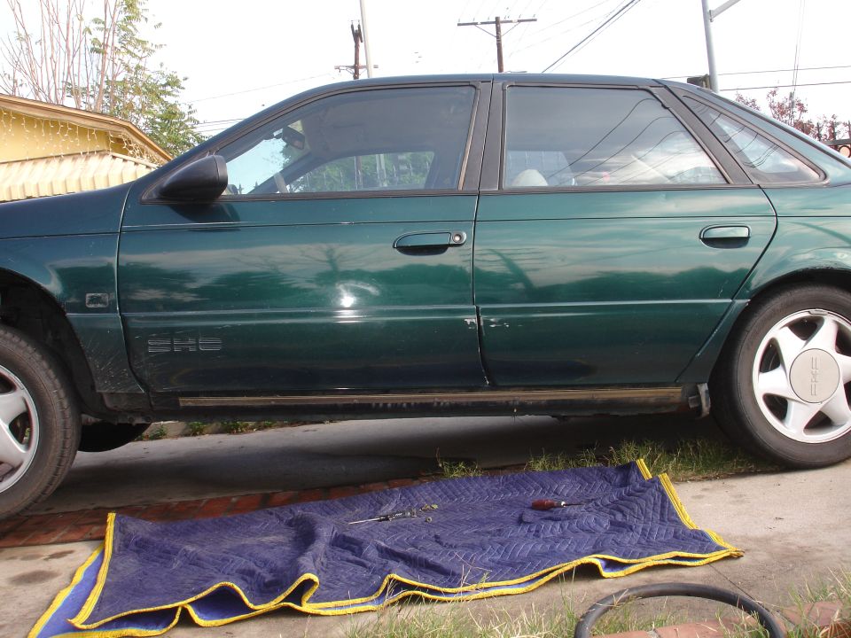 side view of green 1995 Ford Taurus, tools on blanket in front of it