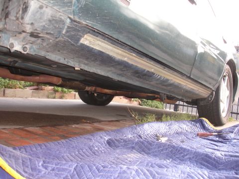 1995 Ford Taurus - The undercarriage of a green vehicle shows signs of rust and wear, with a blue blanket laid out below.