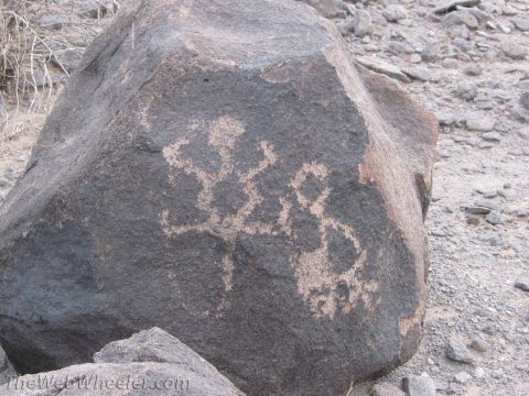 1996 Ford C-350 (Centurion Conversions) - Ancient petroglyphs etched into a dark rock in a desert landscape.