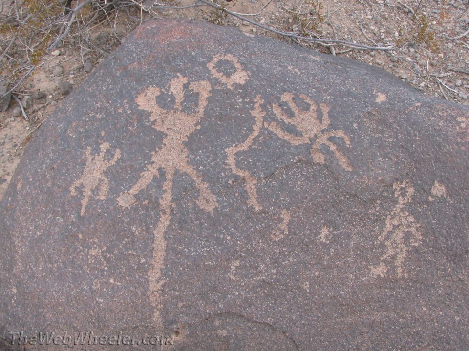 Petroglyphs of human-like figures and a circle on a dark rock surface