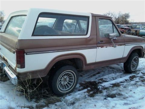 1985 Ford Bronco - Rear three-quarter view of a 1985 Ford Bronco in a junkyard setting with snow on the ground.