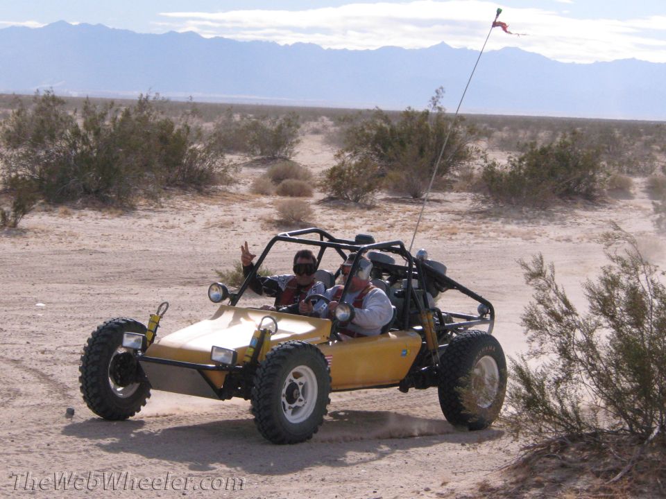 Yellow dune buggy with two people driving on a dirt road in the desert
