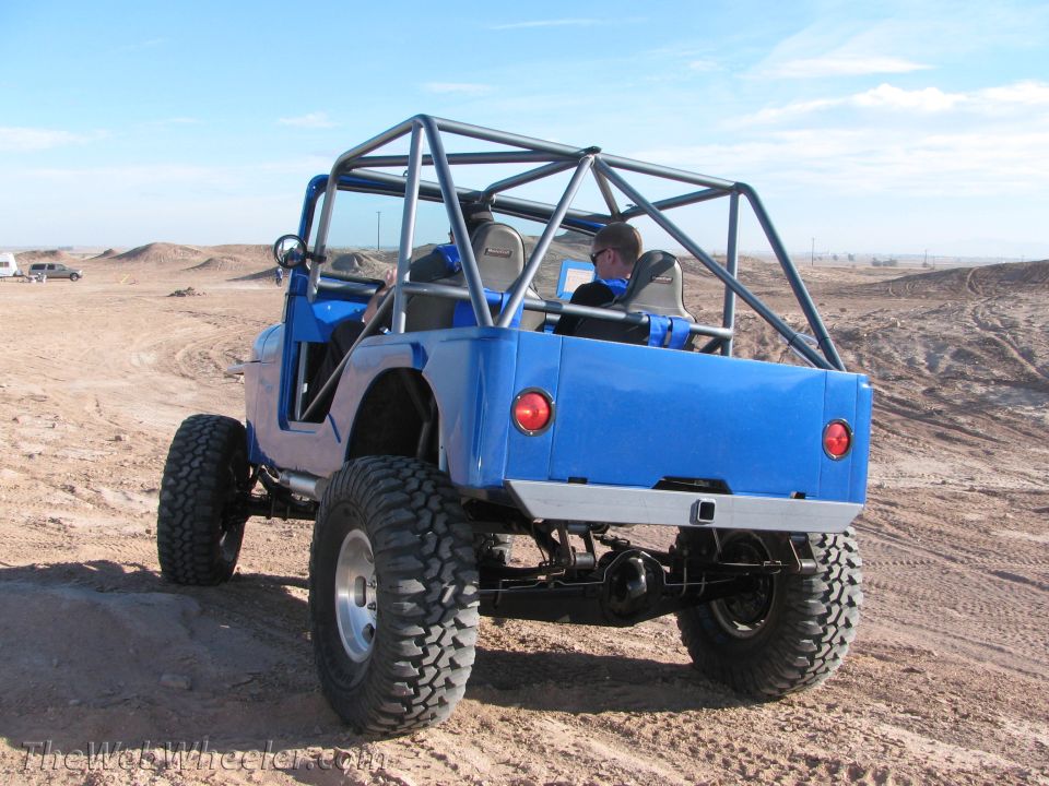 Blue off-road jeep with roll cage, large tires, and custom rear bumper, seen from the rear