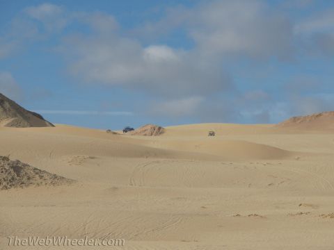 1996 Ford C-350 (Centurion Conversions) - Two vehicles traverse sandy desert terrain under a partly cloudy sky.