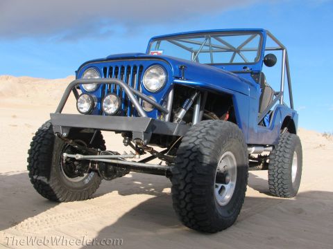 1996 Ford C-350 (Centurion Conversions) - A modified blue Jeep with a roll cage sits in a sandy desert landscape under a blue sky.