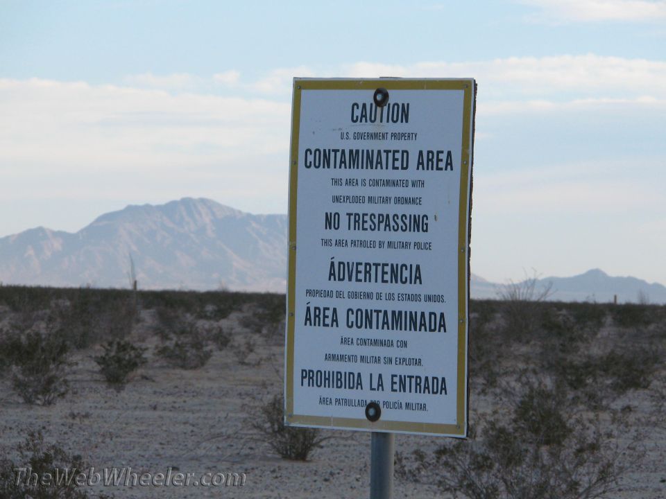 Desert warning sign for contaminated area with unexploded military ordnance, mountains behind
