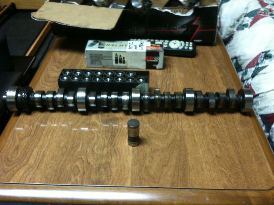 Camshaft and lifters on a wooden table with a box of parts and a remote control